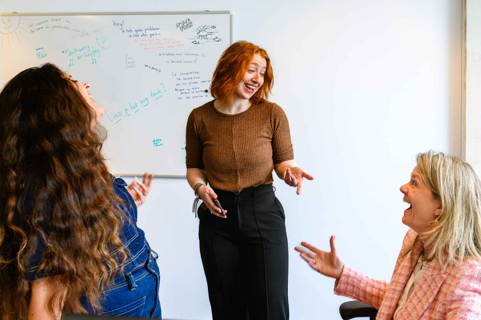 Een moment van samenwerking en plezier! Drie lachende medewerkers in overleg met hun leidinggevende aan het bureau.